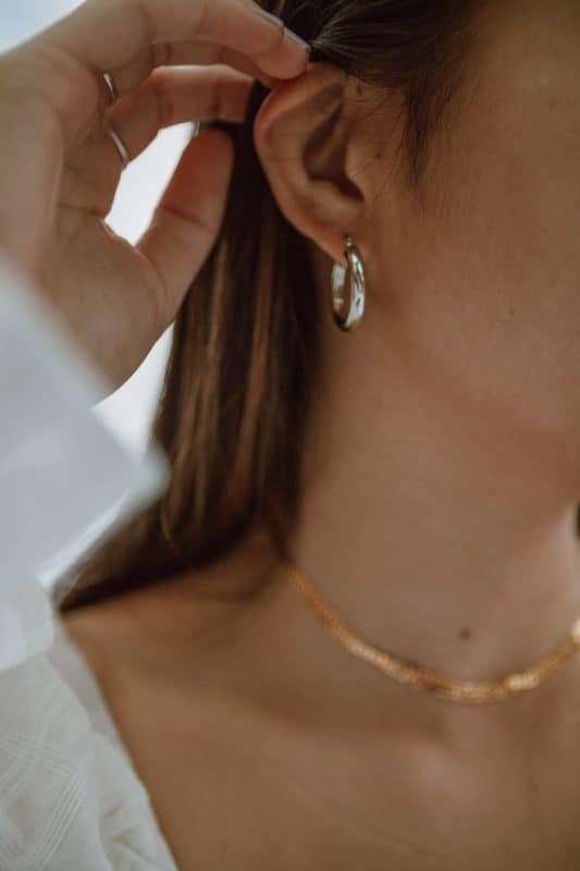 Free Crop unrecognizable female in white dress and elegant earrings touching hair in daytime Stock Photo